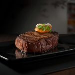 Gegrilltes Steak auf schwarzer Platte mit Garnitur.