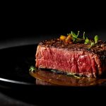 Rindersteak medium-rare mit Kräutern auf schwarzer Platte.