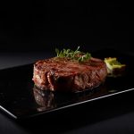 Rindersteak auf dunkler Platte mit Garnitur.