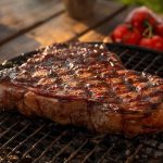 Gegrilltes Steak auf dem Grillrost, Tomaten im Hintergrund