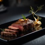 Saftiges Steak in Scheiben auf schwarzer Platte, garniert.