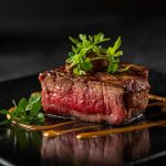 Saftiges Steakstück auf schwarzem Teller mit Kräutern.