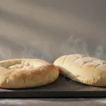 Frische Brotlaibe auf schwarzer Steinplatte, Dampf steigt.