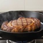 Steak brät in gusseiserner Pfanne über Gasfeuer.