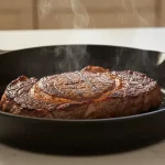 Rindersteak brät in Pfanne, Dampf steigt auf.