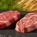 Zwei Ribeye-Steaks mit Marmorierung auf schwarzer Platte.