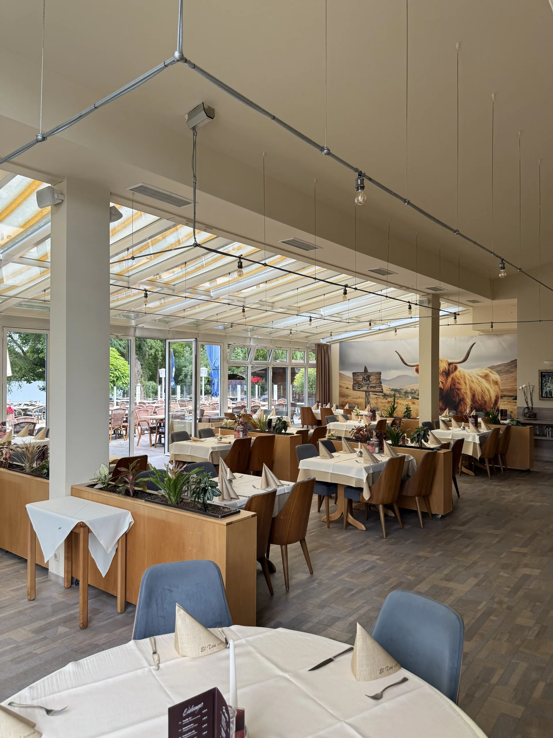 Helles Restaurantinterieur mit weiß gedeckten Tischen und Glühbirnenbeleuchtung.