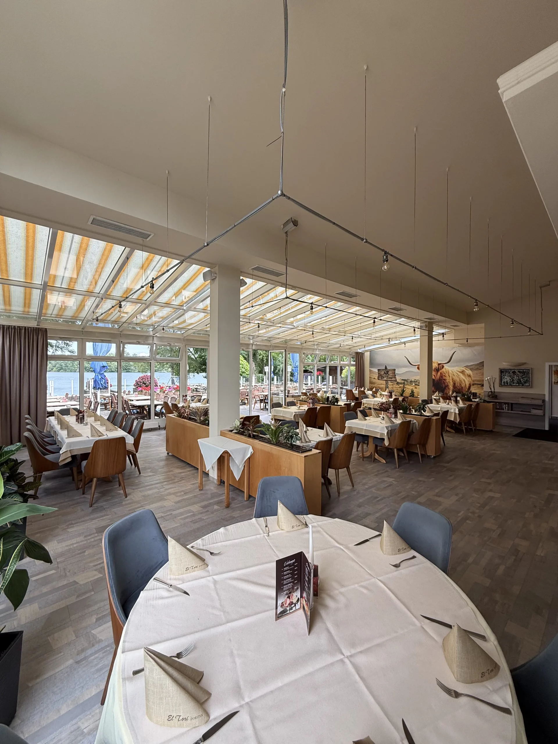 Großer heller Speisesaal mit Tischen, Stühlen und Blick nach draußen.