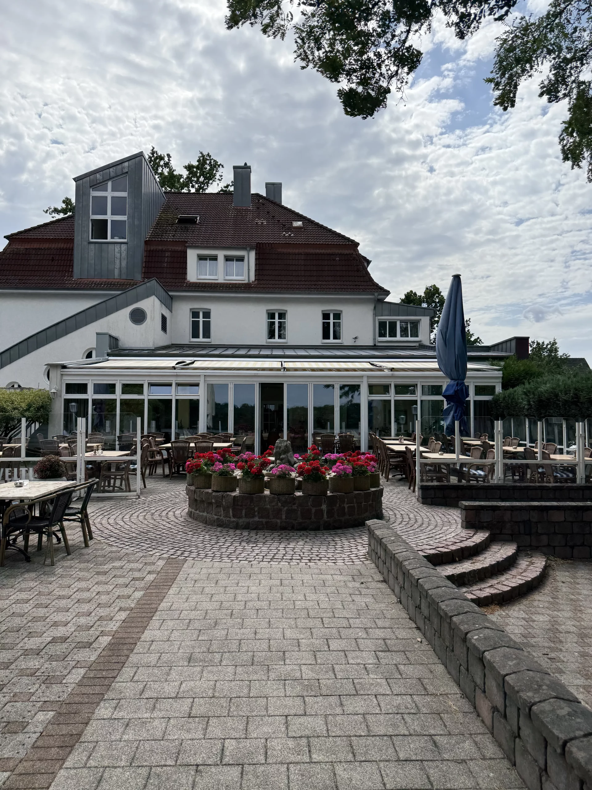 Restaurantterrasse mit Stühlen, Sonnenschirm und Blumenbeet.