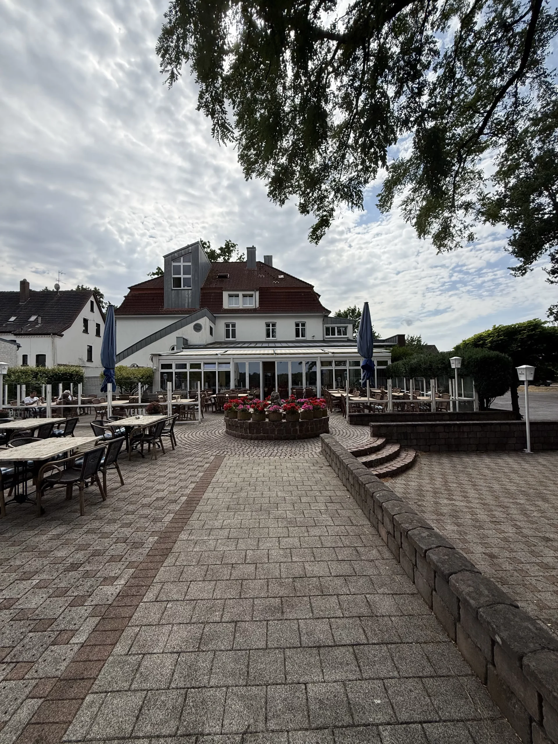 Außencafé mit Tischen, Stühlen und Blumenbeet vor Gebäude.
