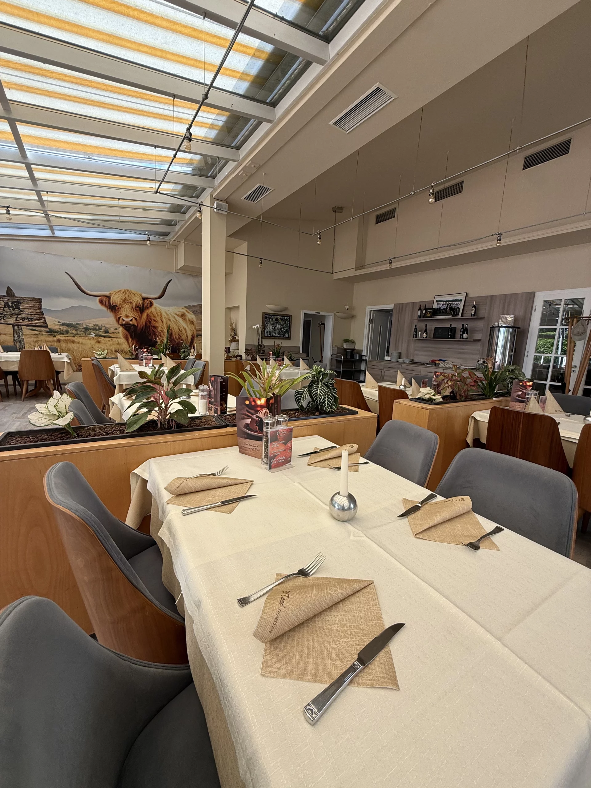Helles Restaurant mit langen Tischen und Kuhwandbild.