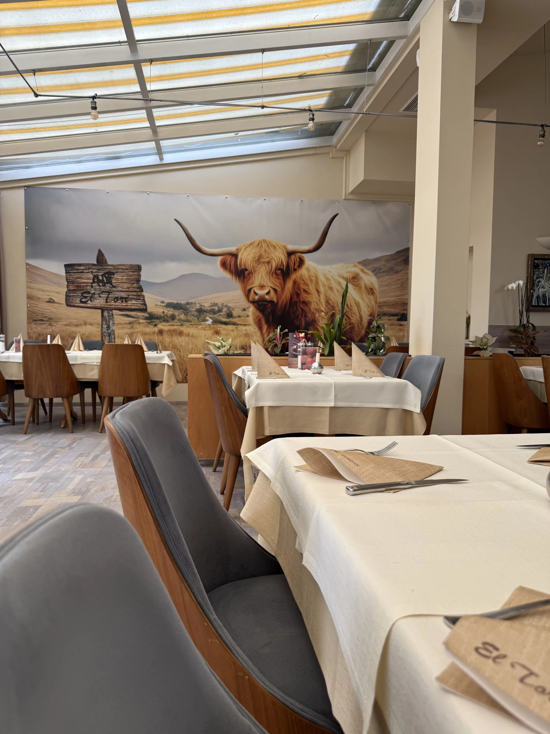 Große Hochlandkuh-Wandmalerei hinter Esstischen im Restaurant