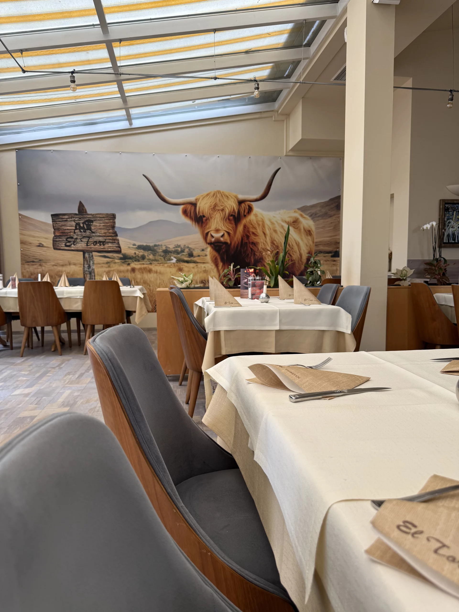 Restaurant mit großer Kuh-Wandmalerei und gedeckten Tischen.