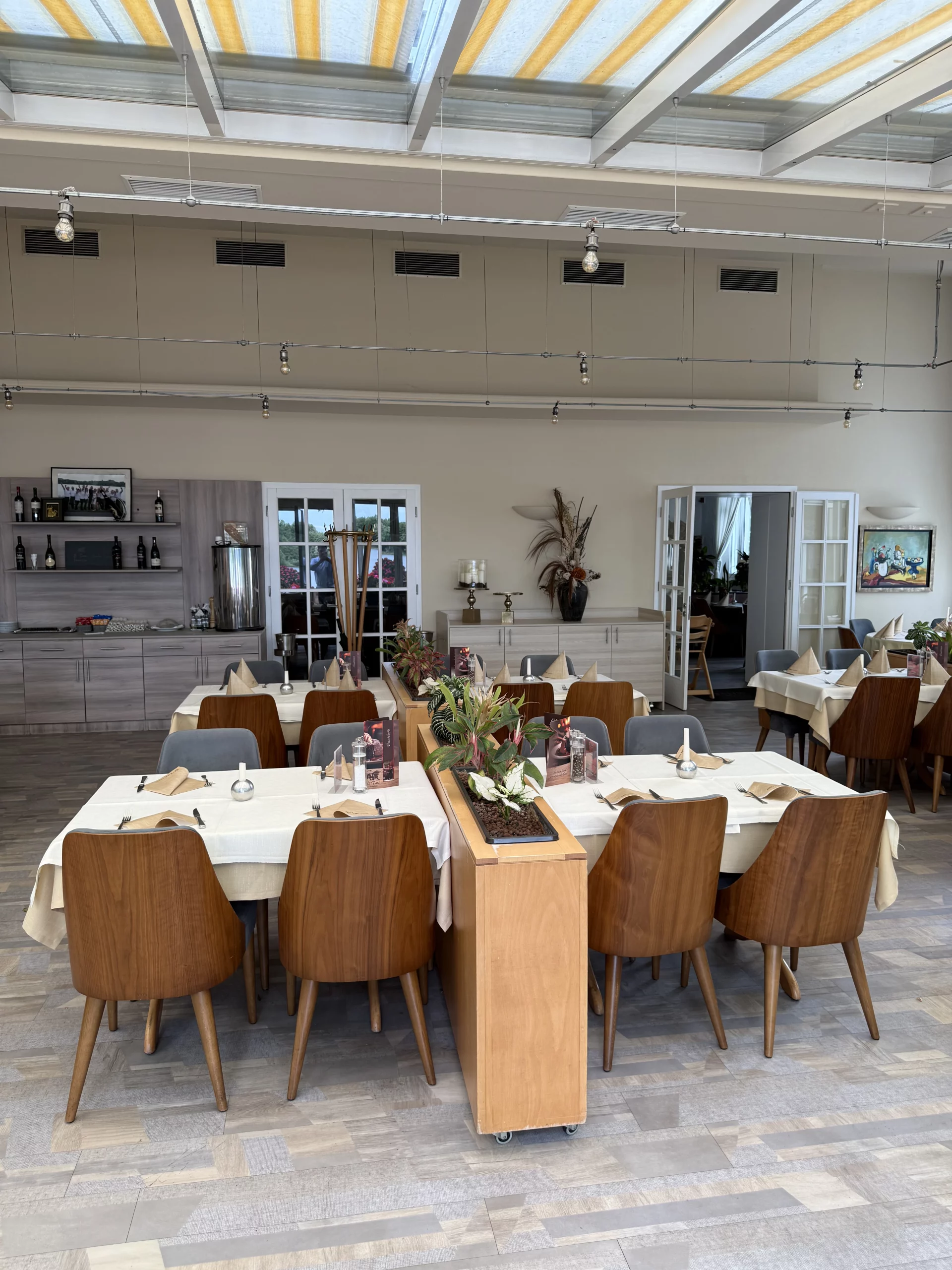 Heller Restaurantsaal mit langen Tischen, Hängeleuchten und Pflanzen