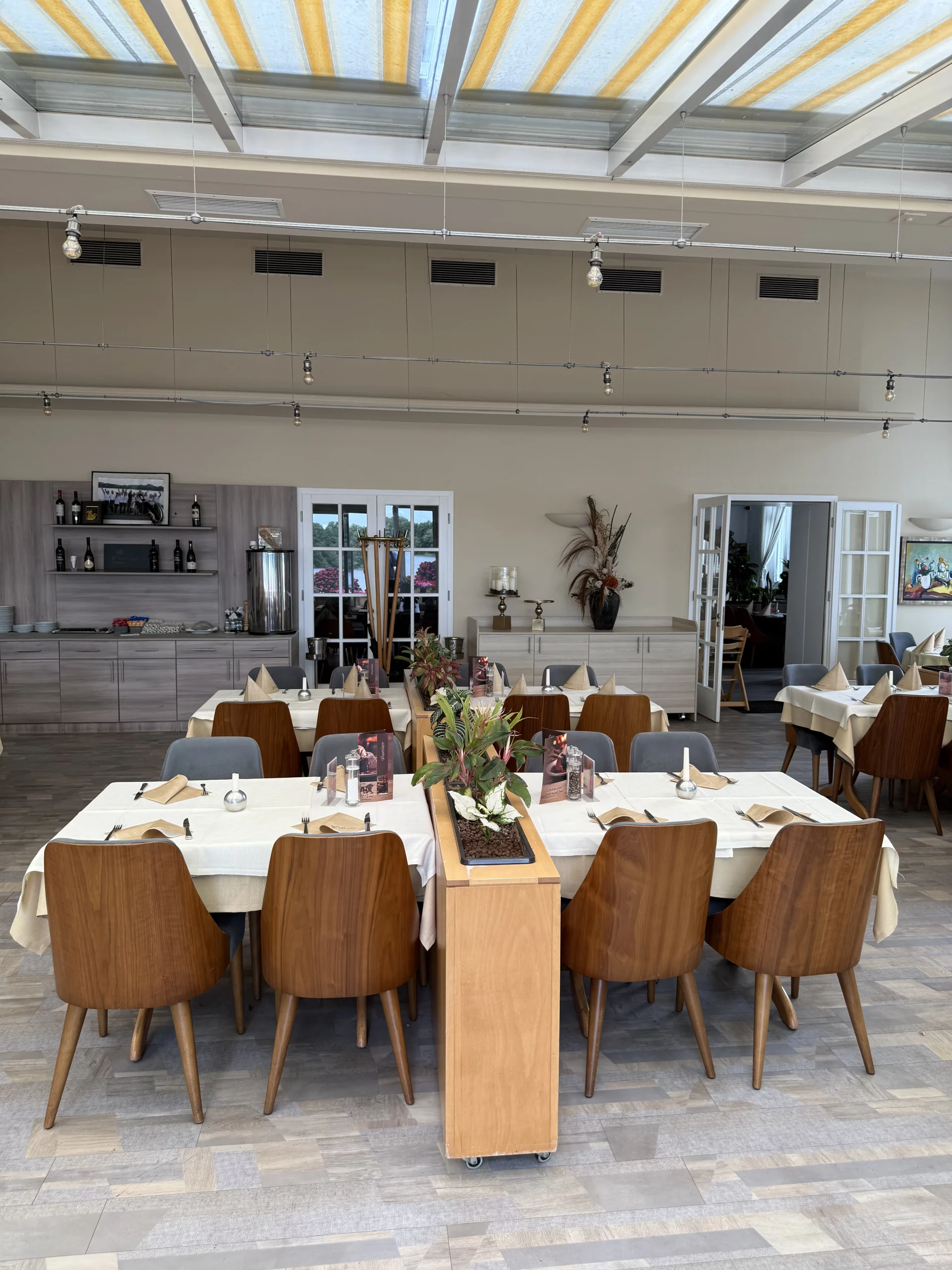 Helles Restaurant mit langen Tischen, Stühlen und Pflanzen.